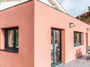 Extension d'une maison au couleur terracotta avec sa terrasse de couleur grise pour un rendu moderne
